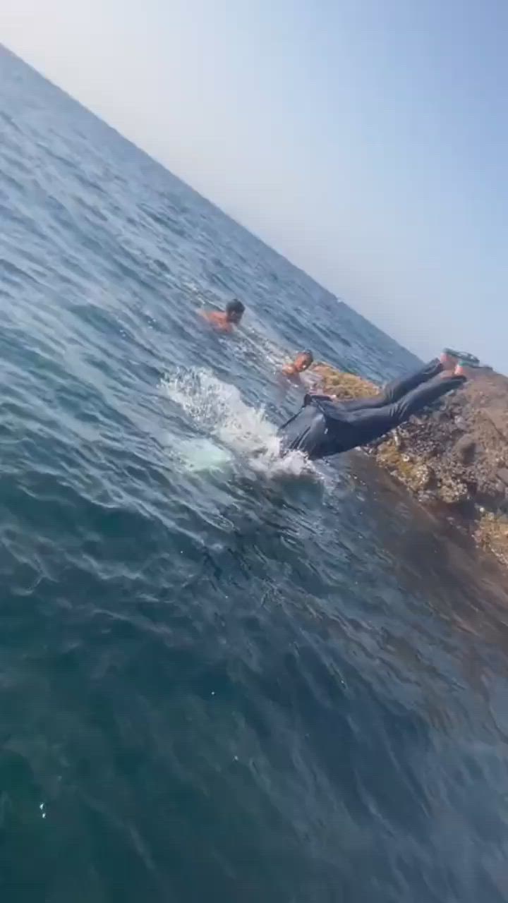 This may contain: a man laying on top of a rock in the ocean next to a body of water