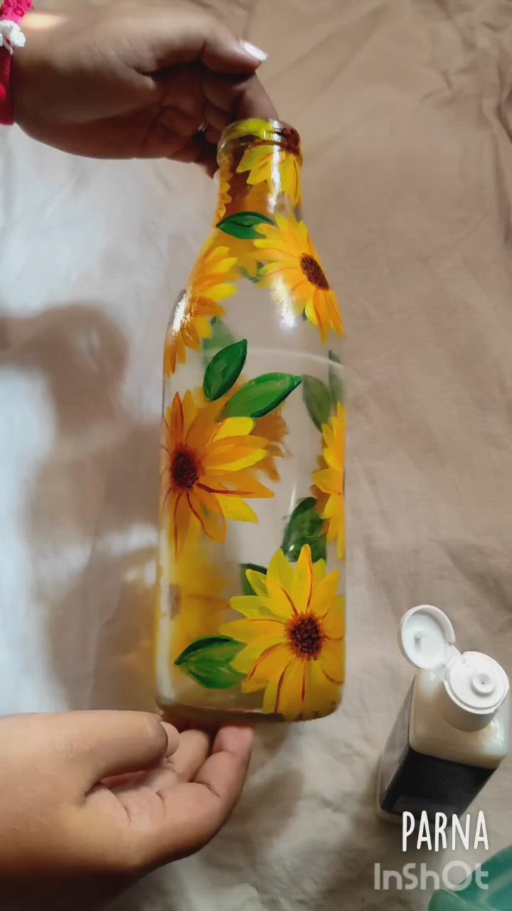 This may contain: a hand holding a glass bottle with sunflowers painted on it