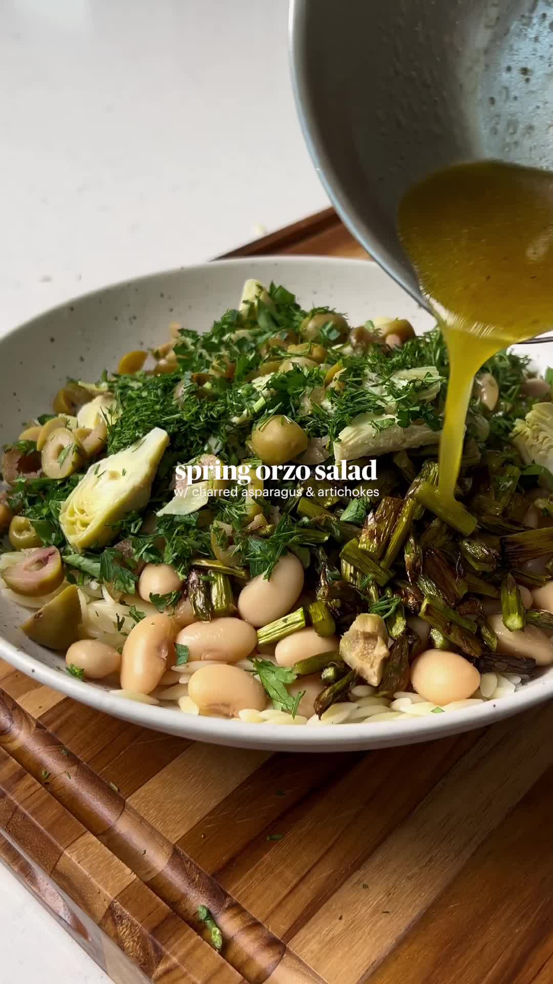 This may contain: a white bowl filled with beans and greens on top of a wooden cutting board next to a spoon