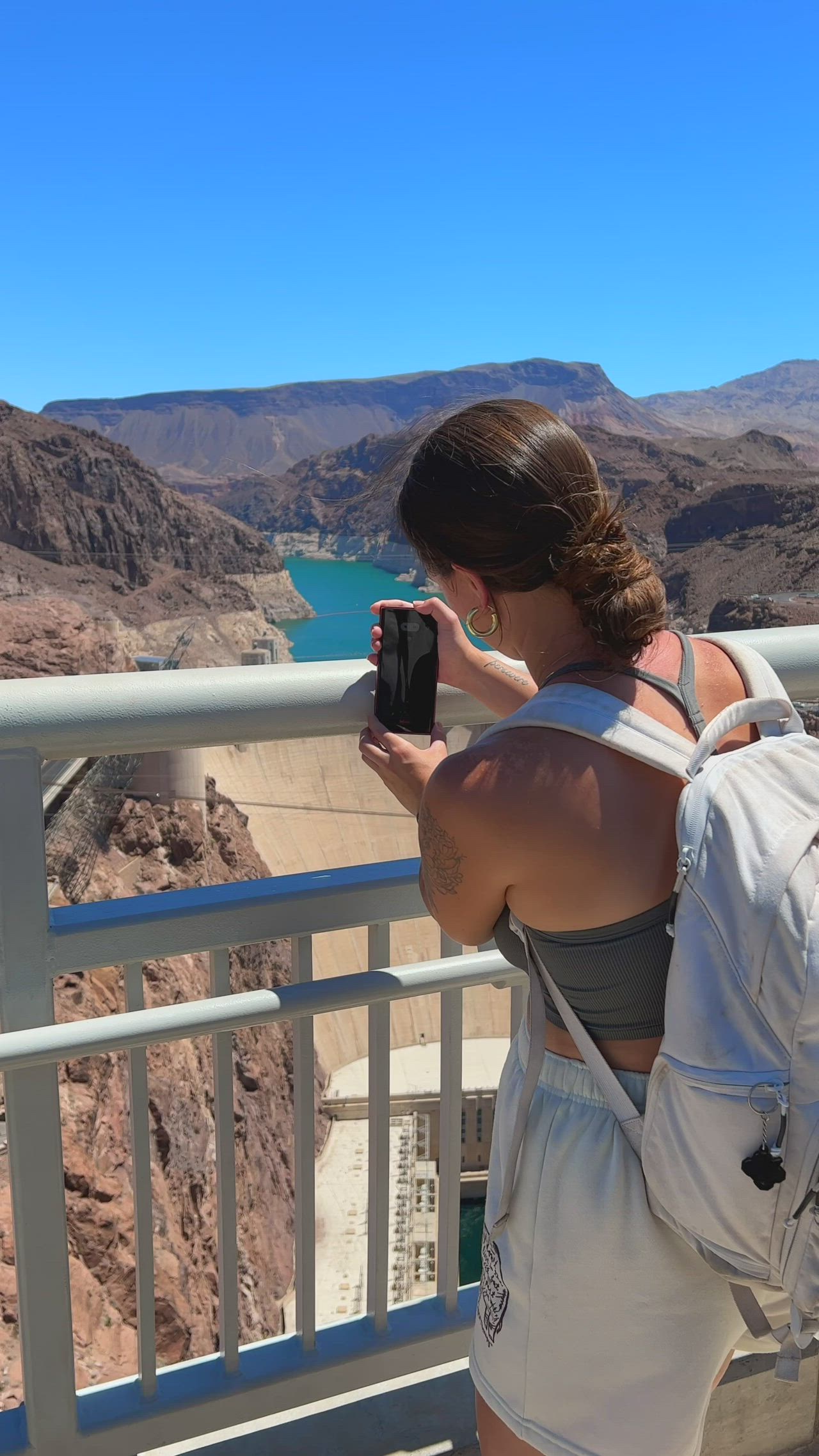 This may contain: a woman taking a photo with her cell phone while standing on a bridge overlooking the mountains