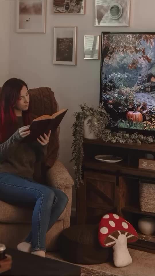 This may contain: a woman sitting on a couch reading a book in front of a tv with mushroom decorations