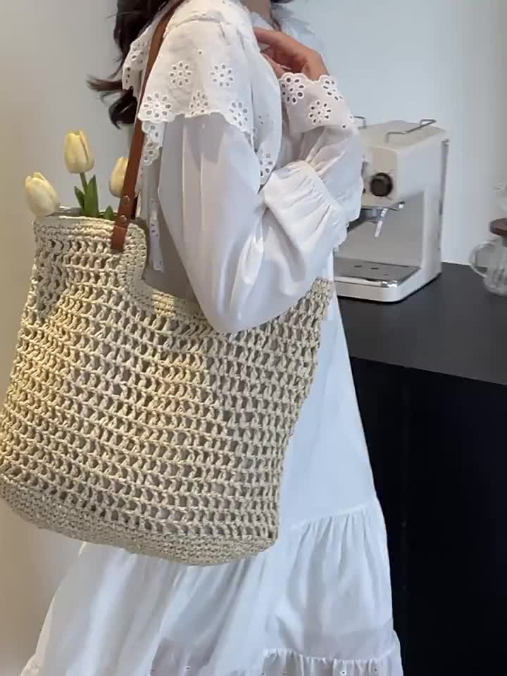 This may contain: a woman in white dress carrying a large woven bag with flowers on the bottom and handles