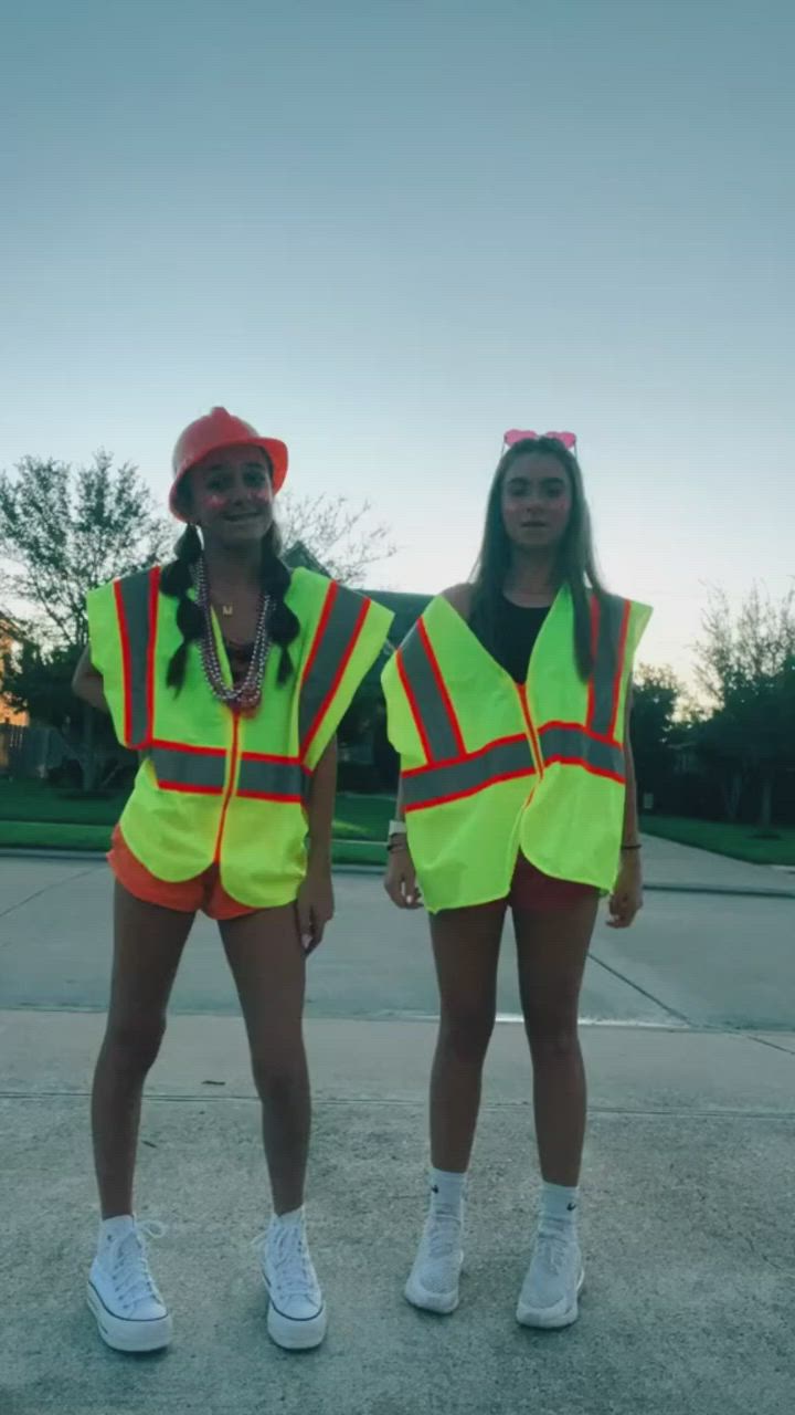 This may contain: two people in safety vests are dancing on the street with their arms raised up