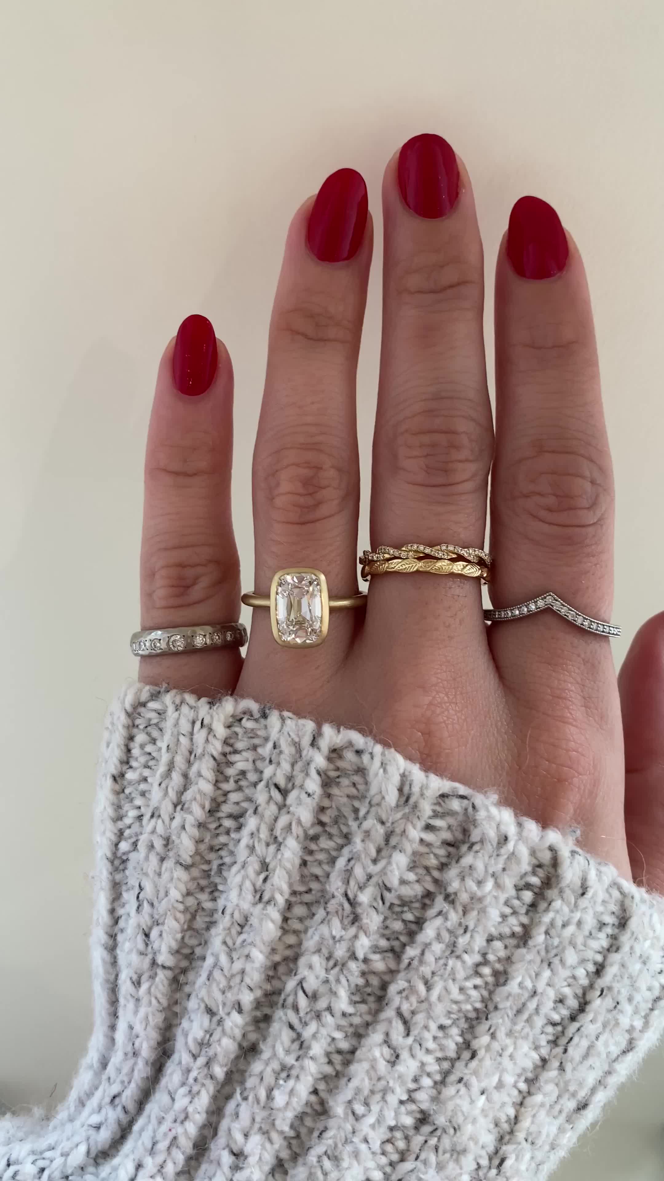 This may contain: a woman's hand with three different rings on her fingers and one is wearing a sweater