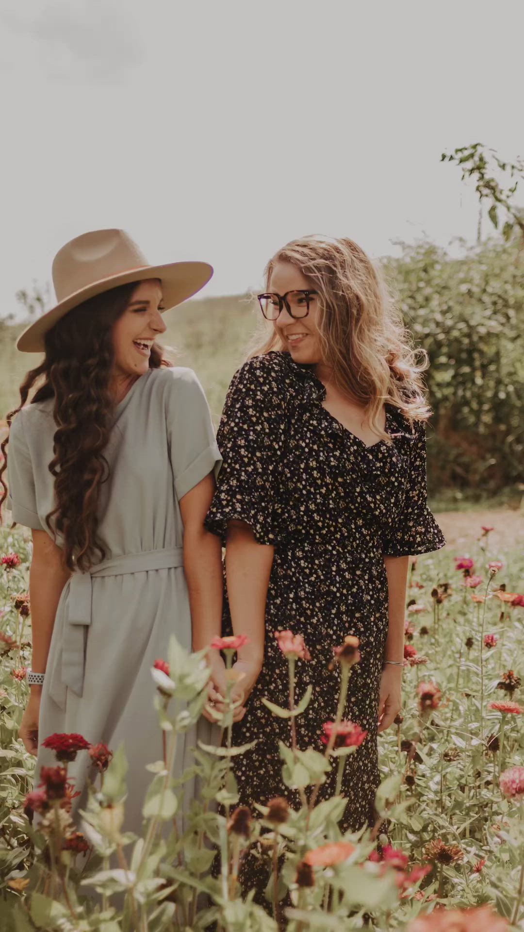 This may contain: two women standing in the middle of a field with red flowers and one wearing a brown hat