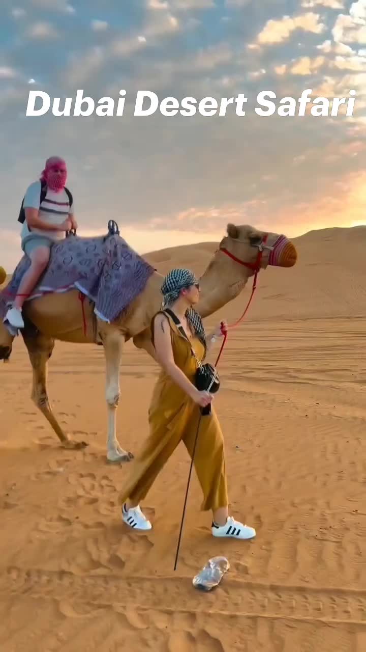 This may contain: two people riding on the back of a camel in the middle of sand dunes, with text that reads dubai desert safari