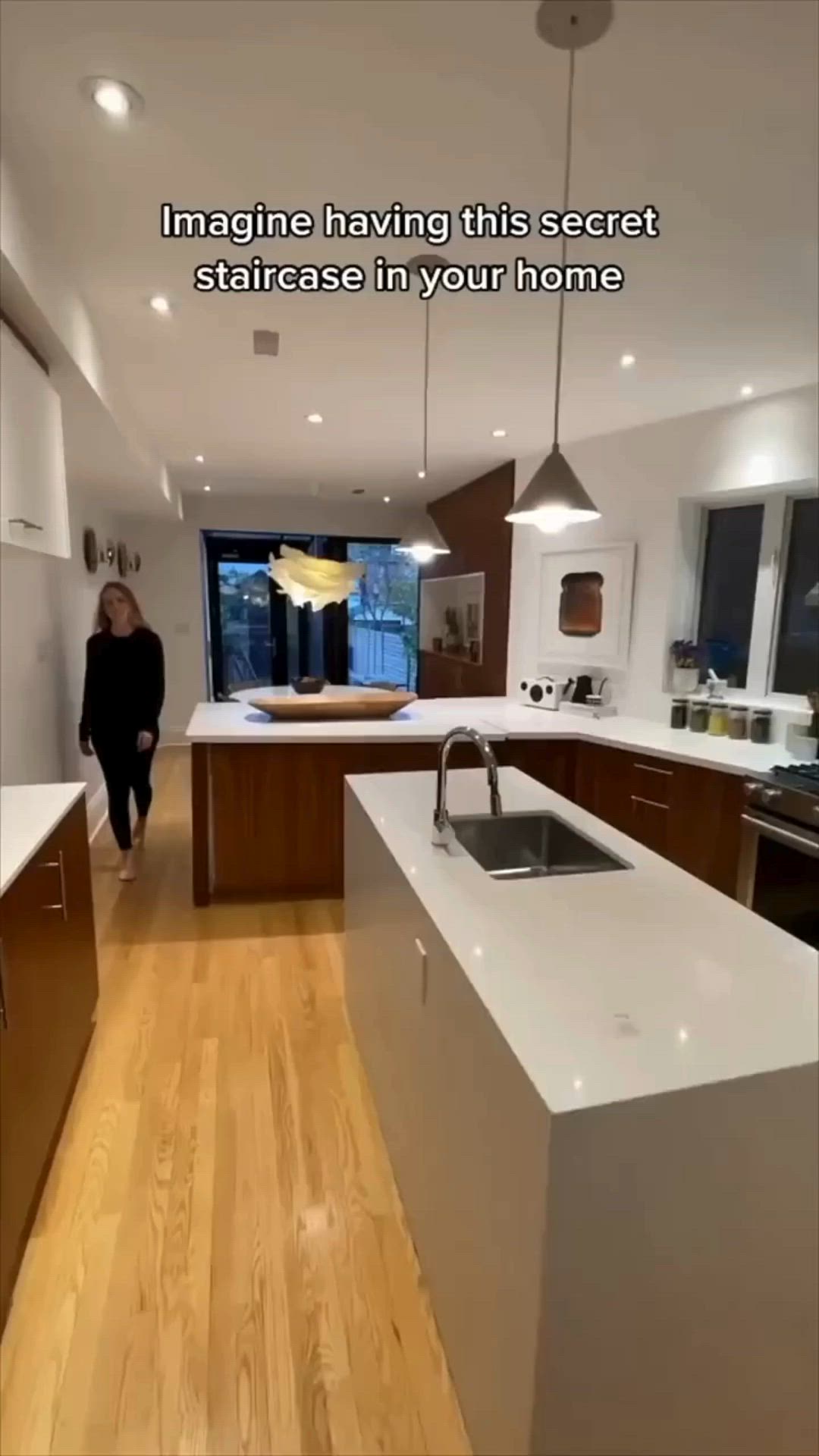 This may contain: a woman standing in a kitchen next to a sink and counter top with the caption imagine having this secret staircase in your home