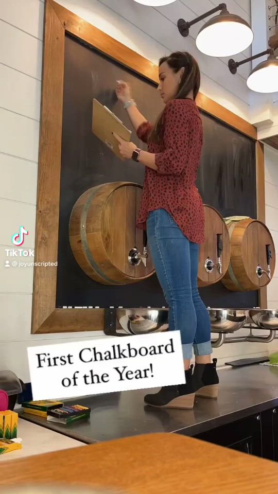 This may contain: a woman standing in front of a blackboard with wine barrels on it