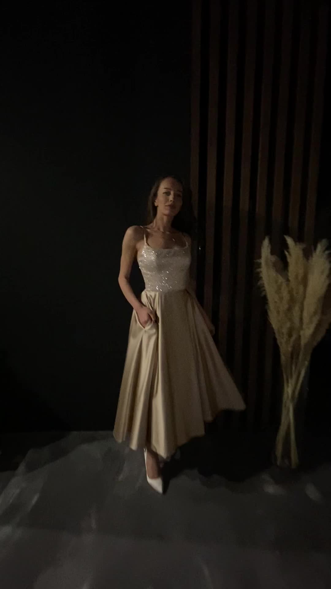 This tea-length dress has a glittering corset with spaghetti straps and a pearly satin skirt. It combines elegance with practicality, including convenient pockets. Important info: The width of the lacing area on the back of the wedding dress can range from 1" to 6", depending on measurements and the level of tightening.