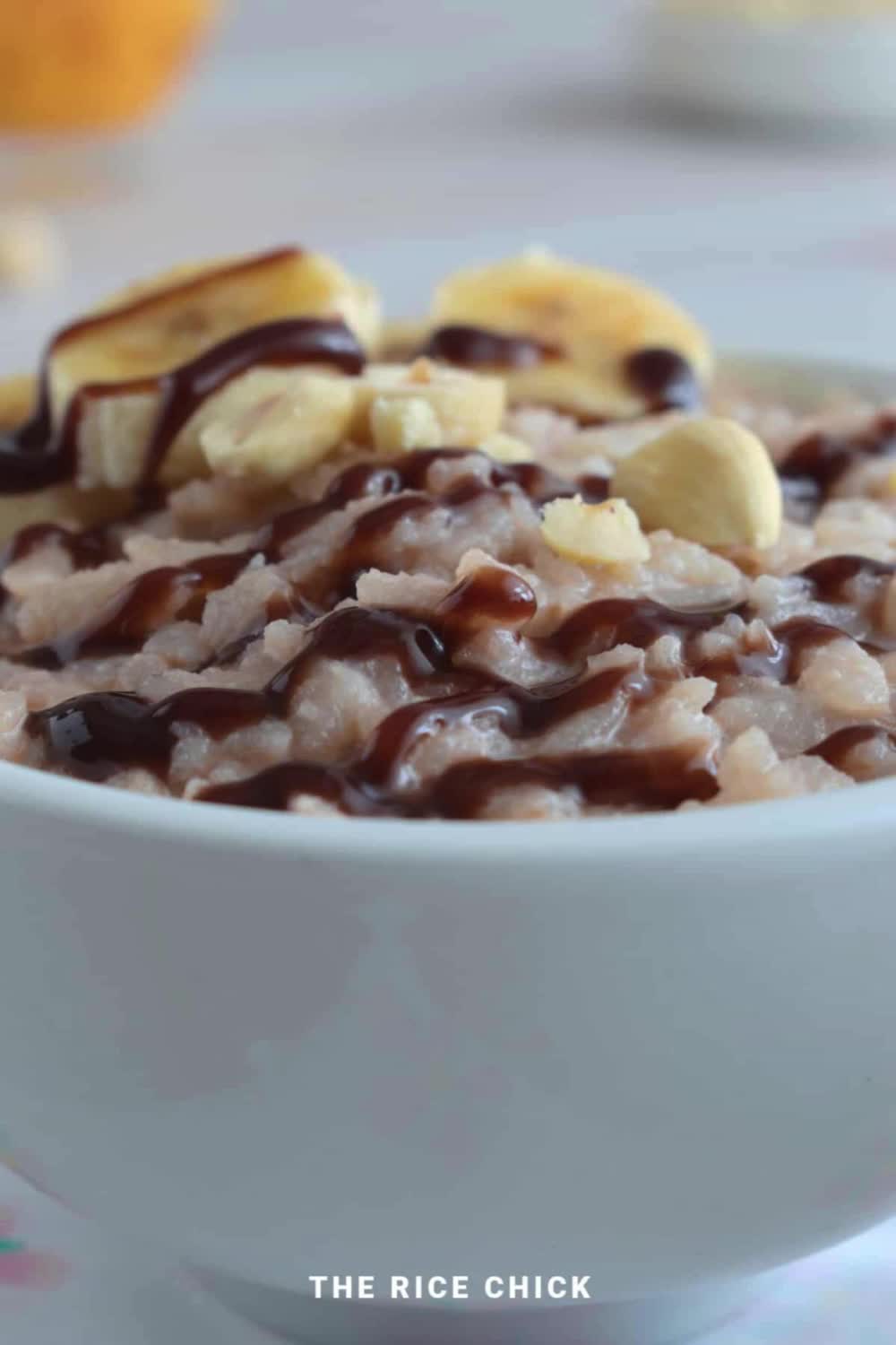 This may contain: a bowl of cereal with nuts and chocolate drizzled on top, next to an orange