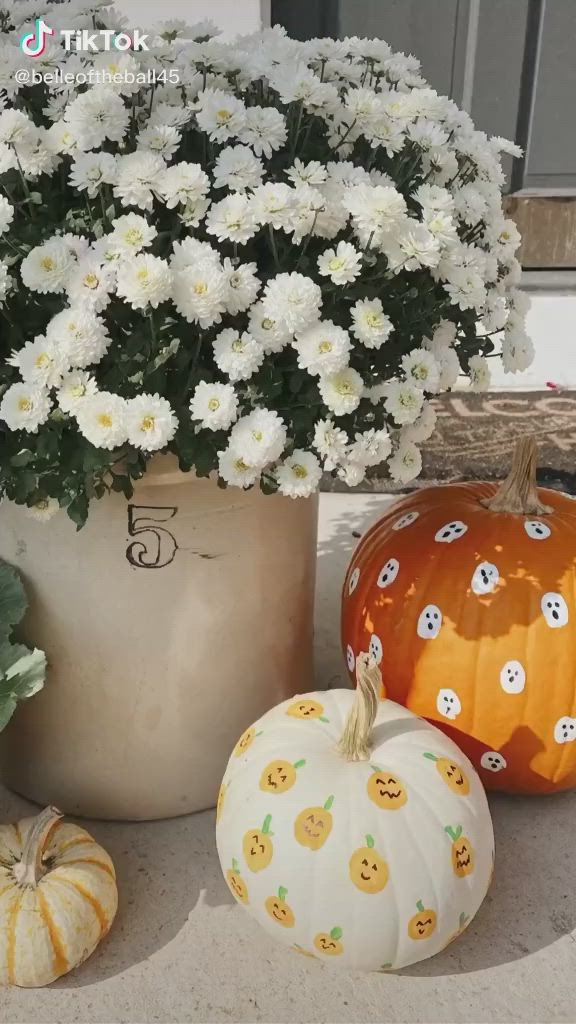 This may contain: a pumpkin decorated with white polka dots and ghost faces is being painted by a person holding a paintbrush