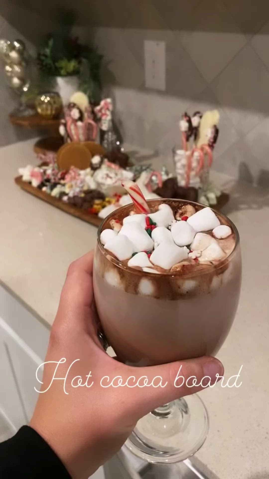 This may contain: someone holding up a hot chocolate drink with marshmallows and candy canes