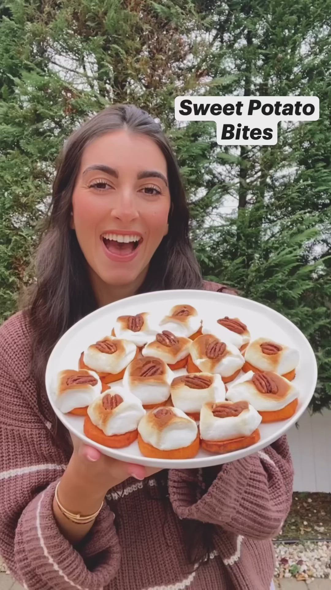 This may contain: a woman holding a white plate filled with mini sweet potato bites covered in marshmallows