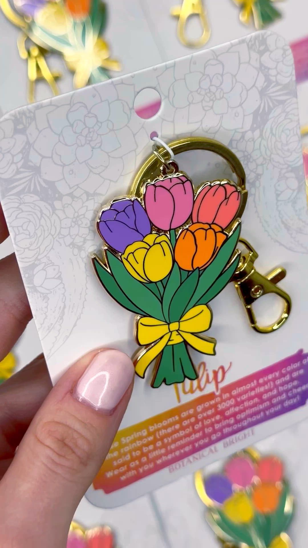 This may contain: a person holding up a flower shaped keychain in front of a bunch of flowers