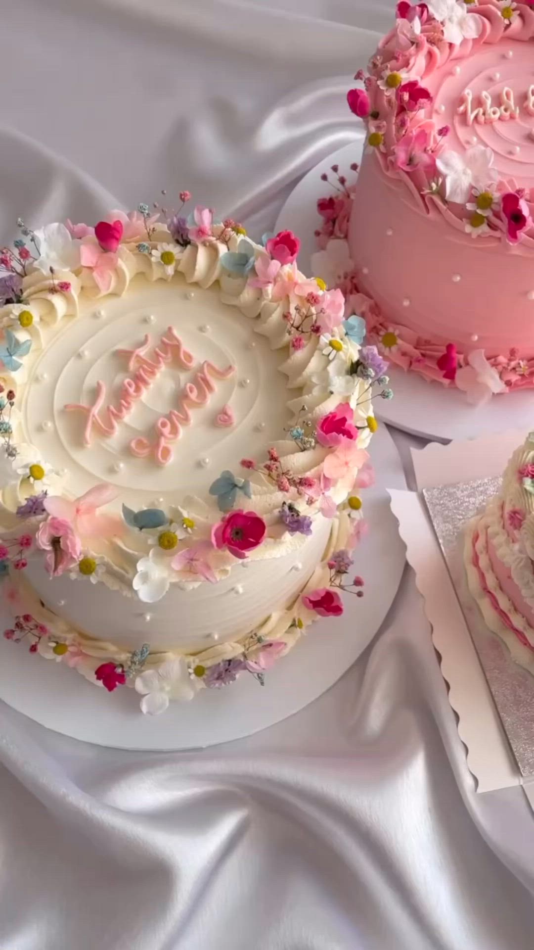 This may contain: there are three cakes on the table with pink frosting and white frosting flowers