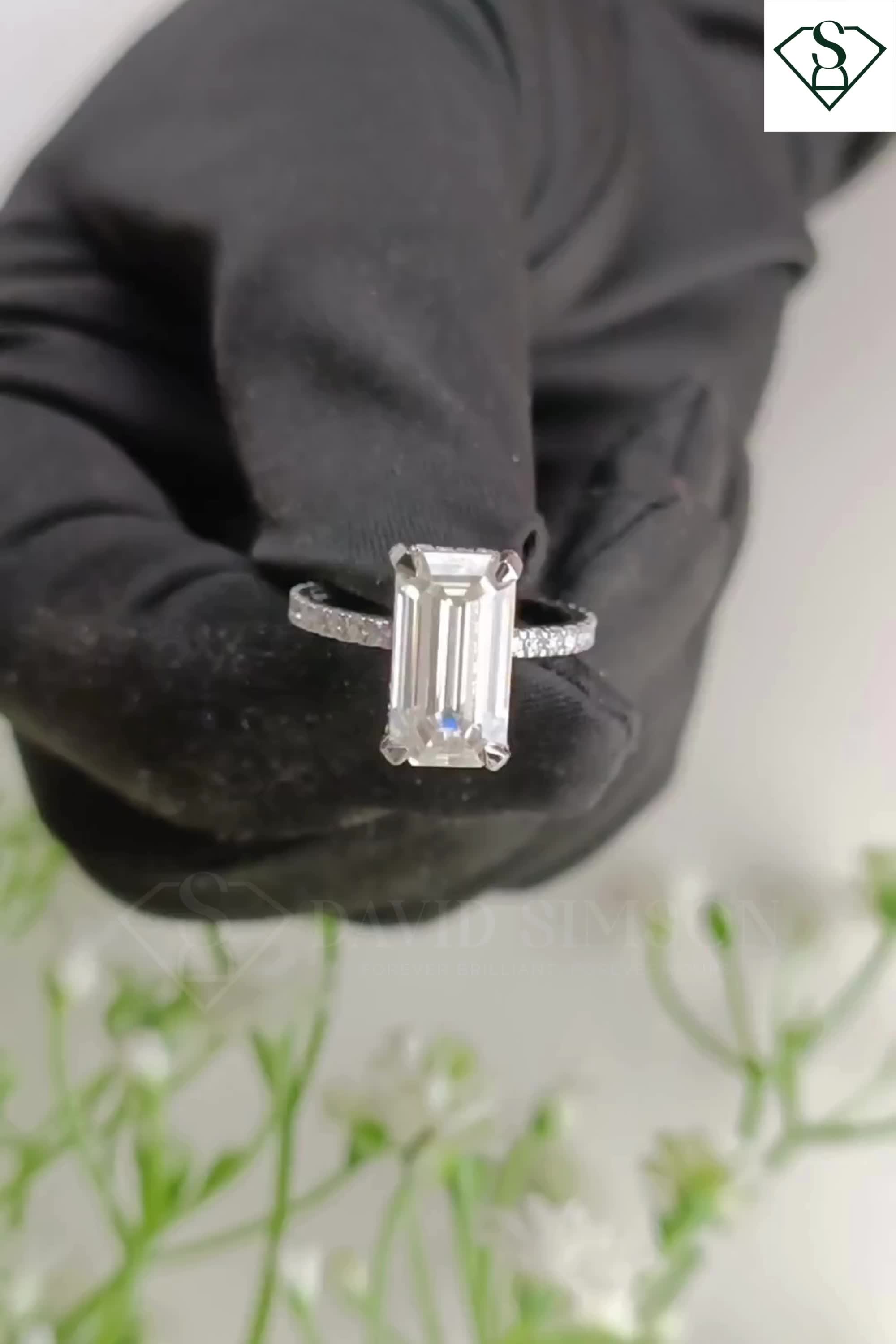 This may contain: an emerald cut diamond ring on top of a black glove with flowers in the background