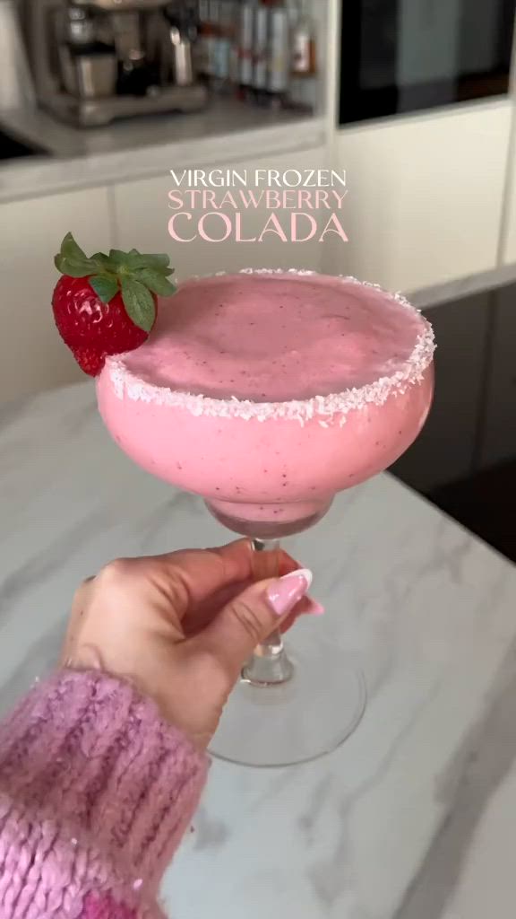 This may contain: a person holding up a pink drink in a glass with strawberries on the rim