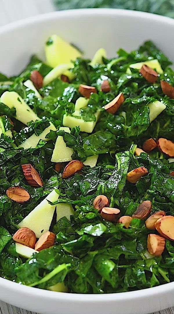 This may contain: kale salad with apples and almonds in a white bowl