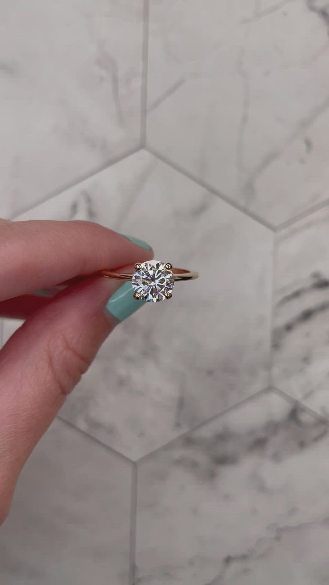 This may contain: a woman's hand holding a diamond ring in front of a white marble wall