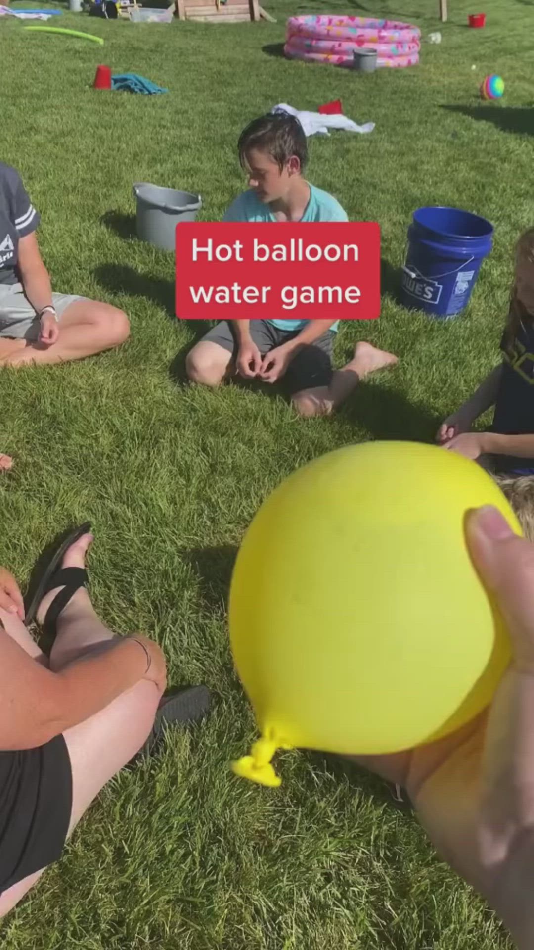 This may contain: people sitting in the grass playing with a yellow frisbee that says hot balloon water game