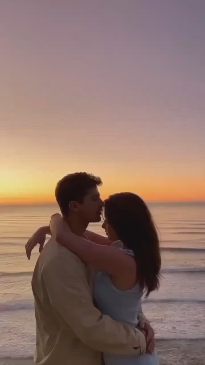 This may contain: a man and woman embracing on the beach at sunset