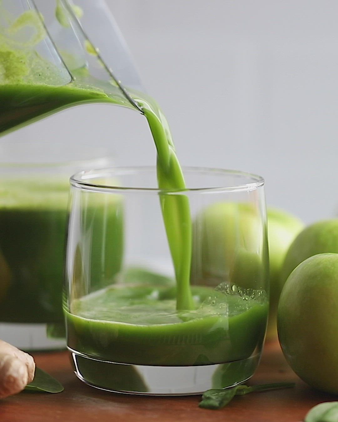 This may contain: green juice being poured into a glass in front of some apples and other fruit on the table