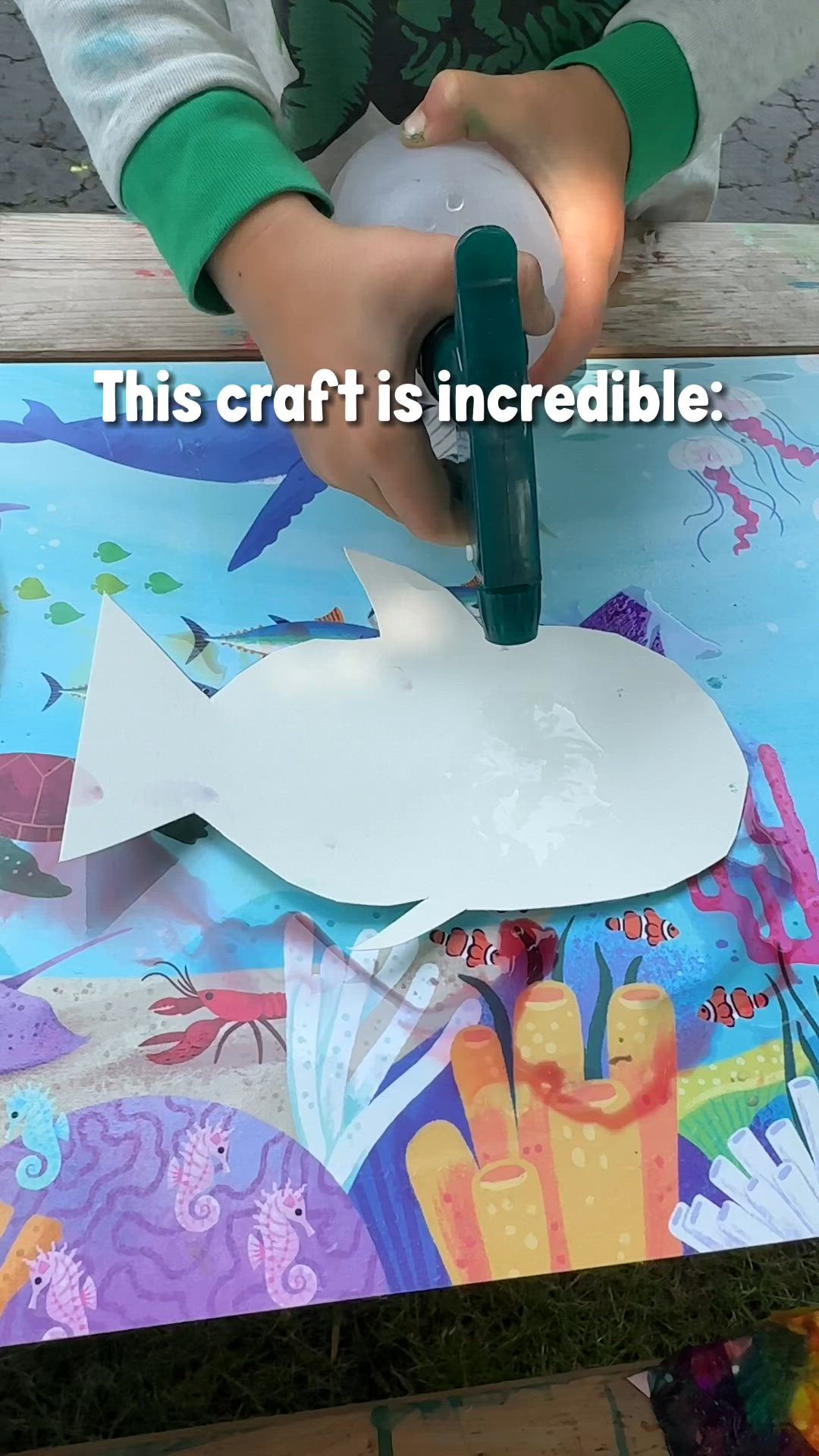 This may contain: a child is making a paper cut out of a shark with glue on it and the caption reads, this craft is incredible