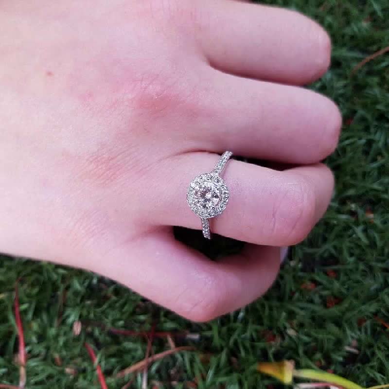 This may contain: a person's hand with a diamond ring on top of their finger and grass in the background