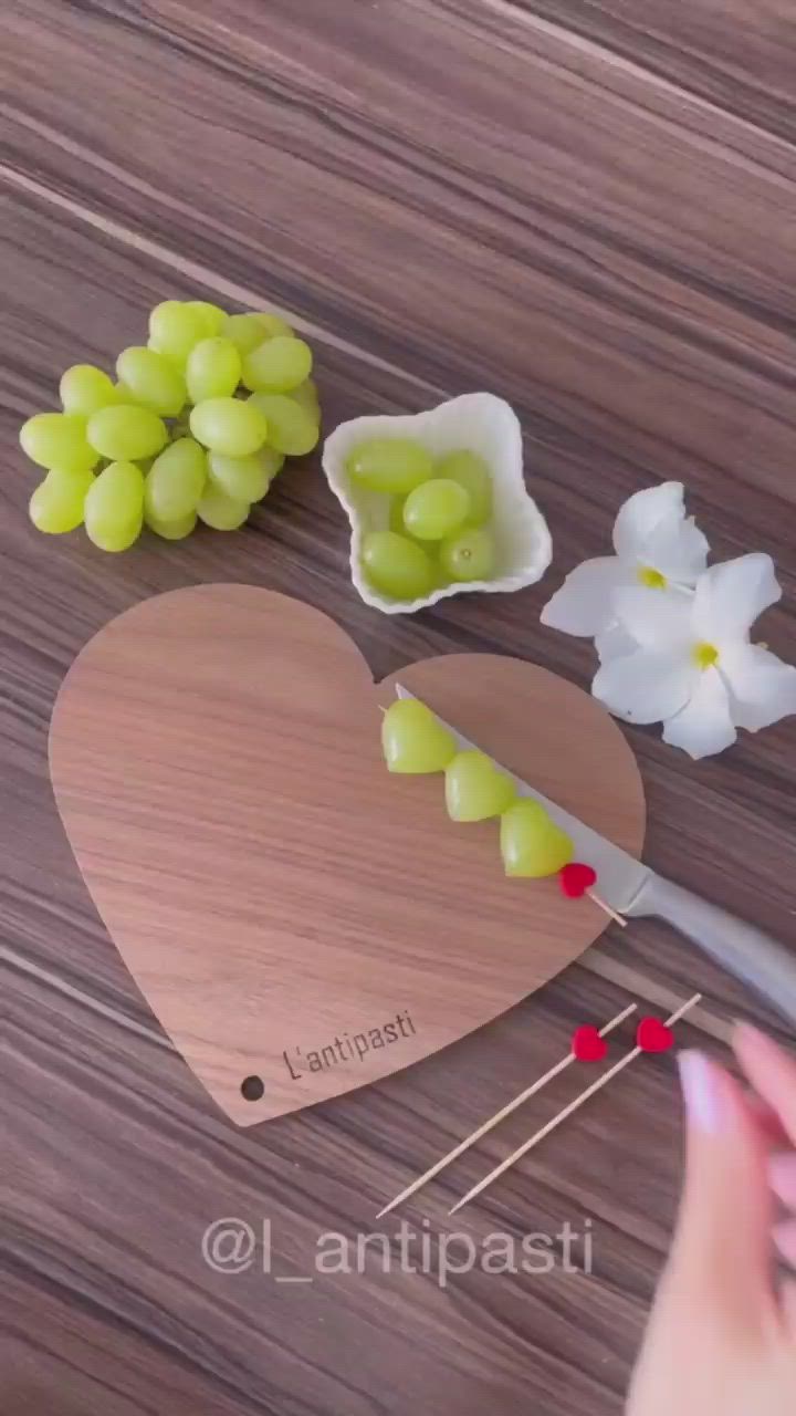 This may contain: a heart shaped cutting board with grapes and flowers on it, next to a pair of scissors