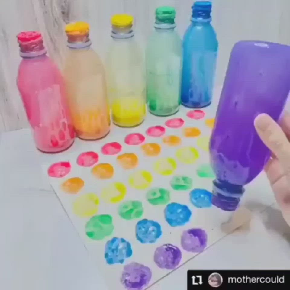 This may contain: a hand is holding an empty bottle in front of several colored bottles on a table