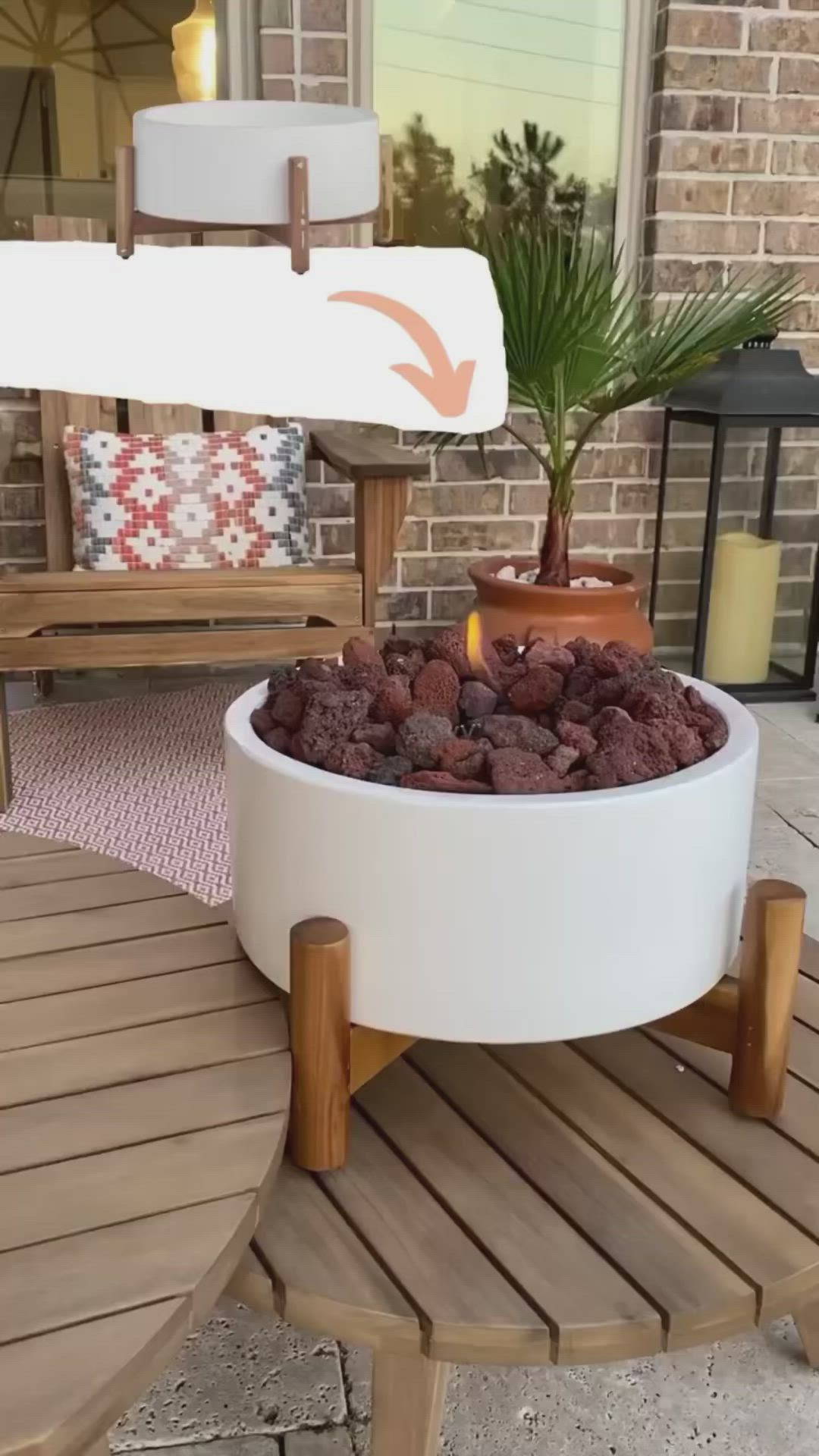 This may contain: a fire pit sitting on top of a wooden table next to a chair and potted plant