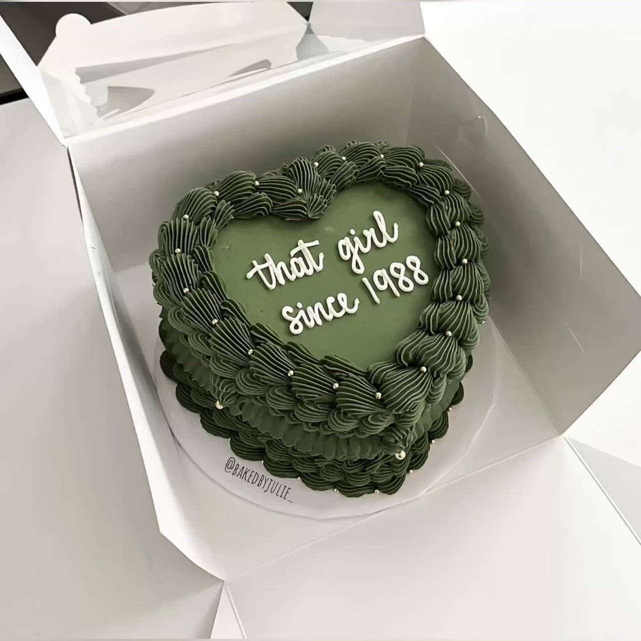 This may contain: a green heart shaped cake in a box