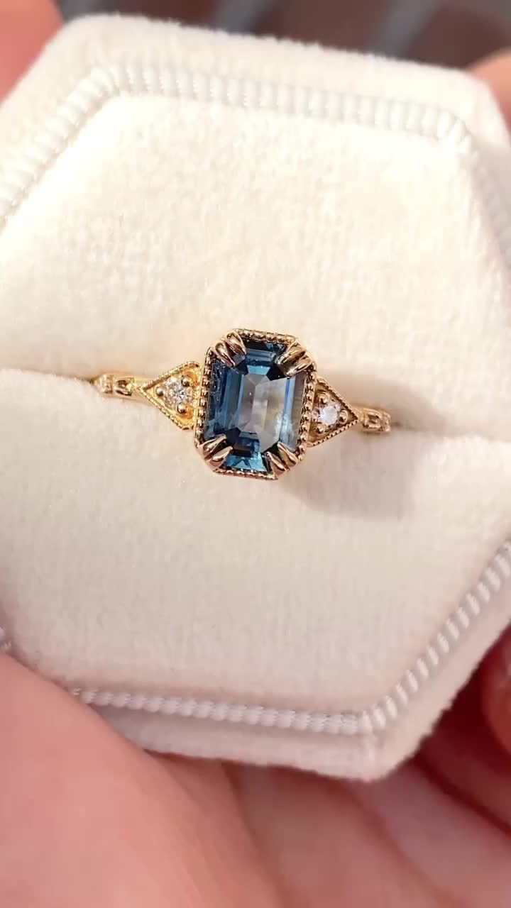 This may contain: a woman's hand holding an engagement ring with a blue stone