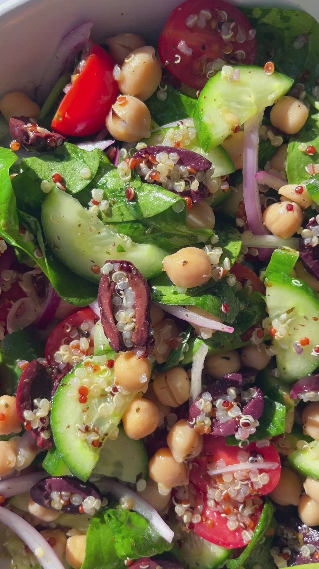 This may contain: a salad with cucumbers, tomatoes, onions and chickpeas in it