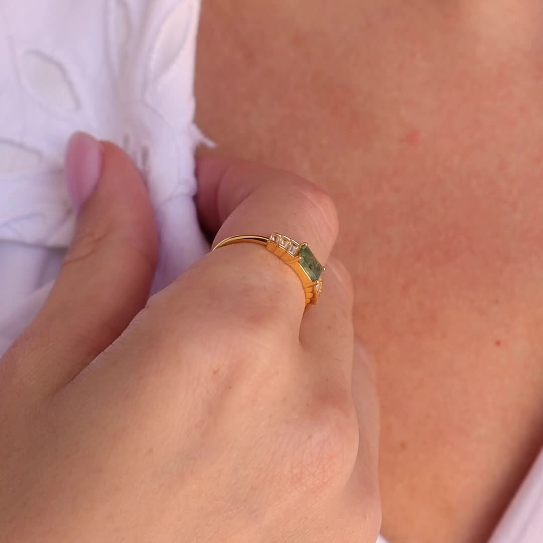 This may contain: a close up of a person wearing a gold ring with green stones on the side