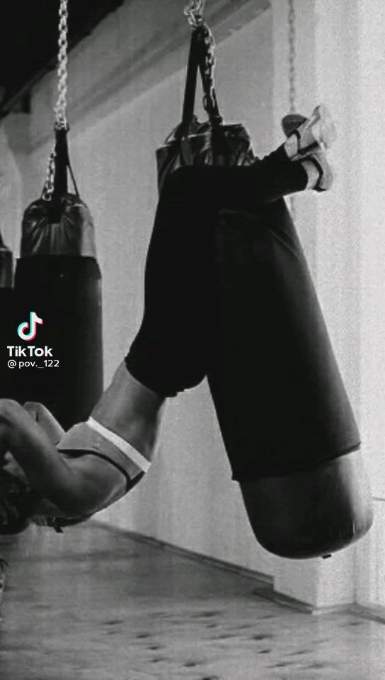 This may contain: black and white photograph of a man wearing boxing gloves hanging from ropes in a gym