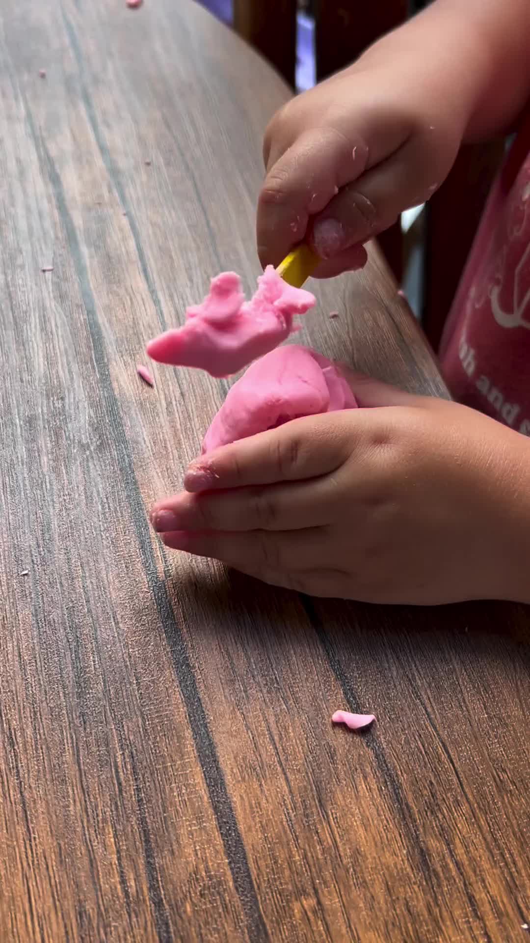 This may contain: a child is playing with pink frosting on a wooden table and it looks like they are having fun