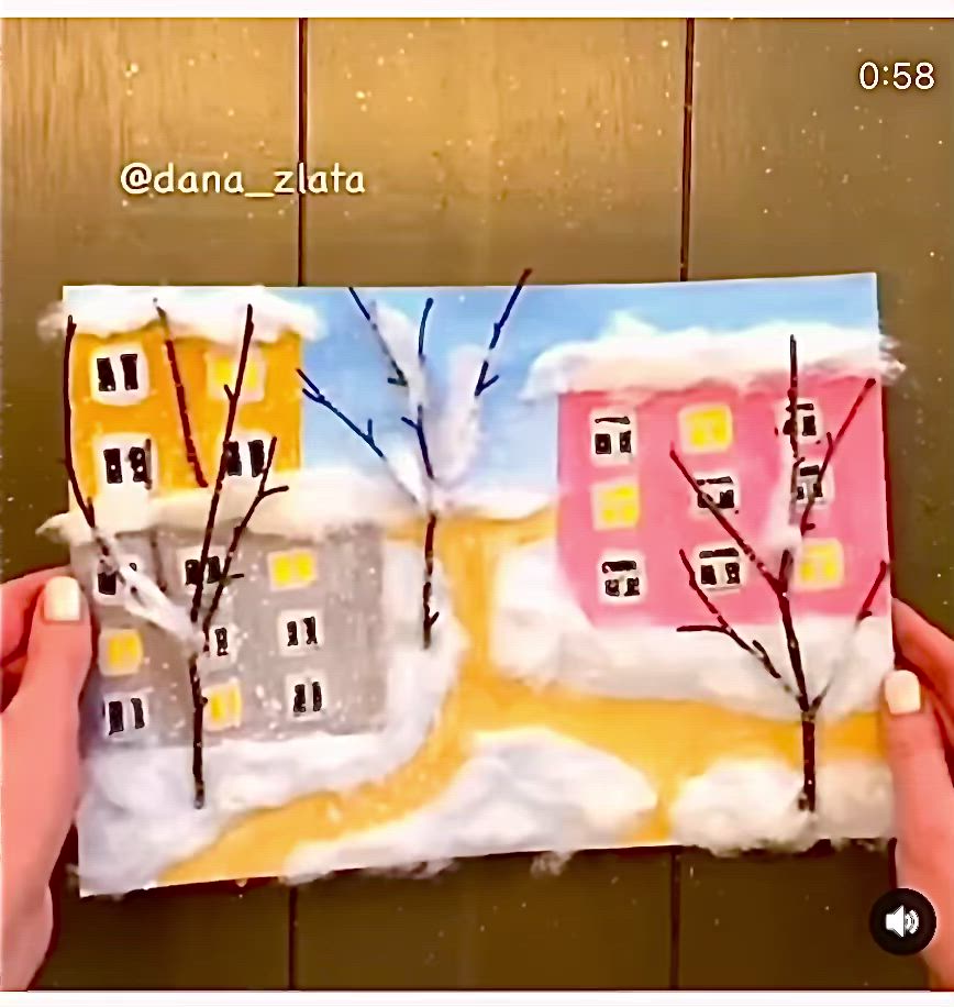 This may contain: someone is holding up a piece of paper with houses and trees painted on it in front of a wooden wall