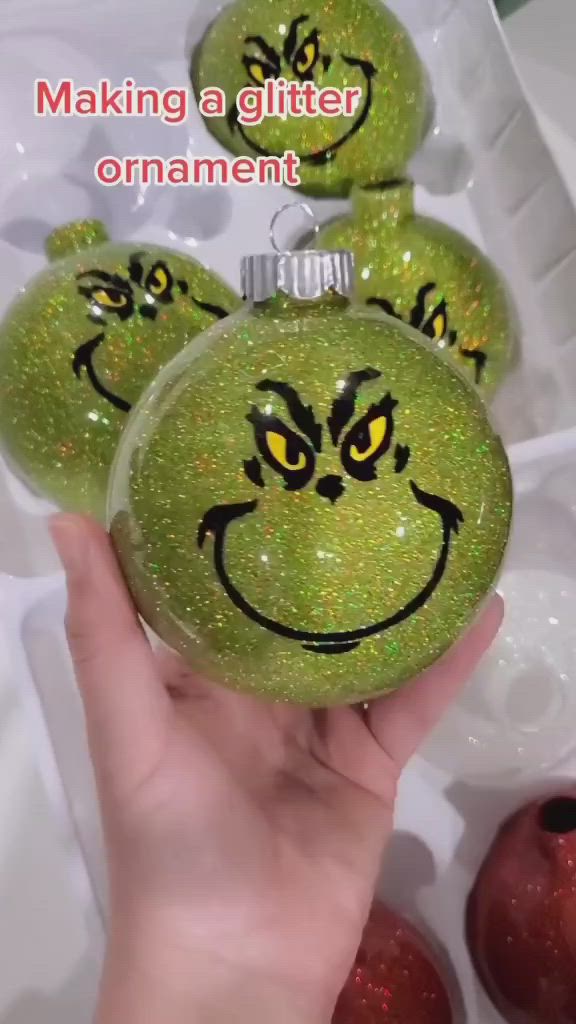 This may contain: a hand holding a green ornament with smiley face drawn on it