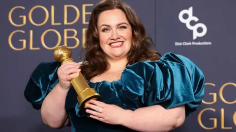 Reuters Jessica Dunning wins a Golden Globe award - she is seen with long brown hair and wearing a blue velvet gown, smiling and holding her award 