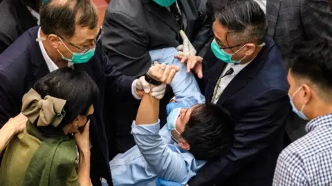 Getty Images A pro-democrat lawmaker is restrained by security guards at the Legislative Council in Hong Kong