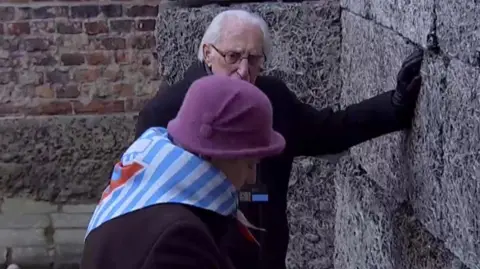 A man and a woman leave a candle by wall in Auschwitz