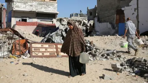 A displaced Palestinian woman, Makram Hamdouna, carries a water container outside her shelter, in Khan Younis in the southern Gaza Strip December 19, 2024. 