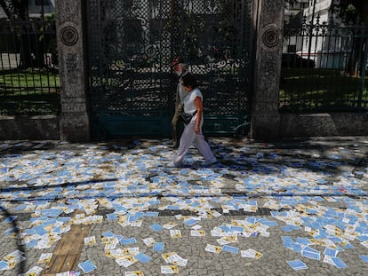 Dos personas caminan por una calle cubierta de folletos de candidatos cerca de una zona electoral, en Río de Janeiro (Brasil).