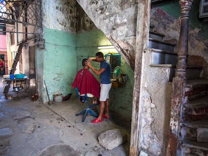 Un barbero realiza un corte bajo las escaleras de su edificio de departamentos en La Havana, Cuba, en una fotografía de archivo.