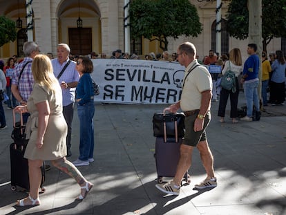 Dos turistas pasan delante de la protesta de colectivos vecinales contra el aumento de los pisos turísticos en Sevilla.