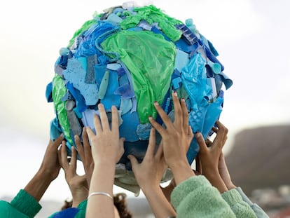 Friends coming together to hold up an art work depicting the world  made from plastic pollution collected on local beaches