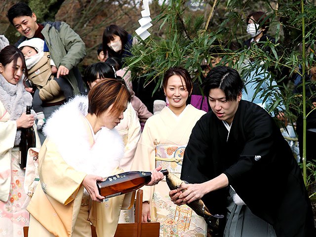 コイにお神酒を飲ませる厄年の男女＝庄川水記念公園