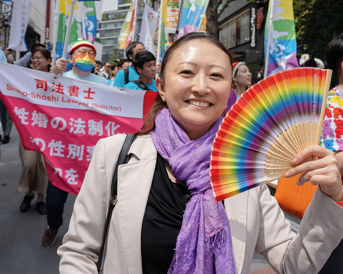 「東京レインボープライド２０２４」に参加、街を練り歩く東友美。性の多様性を象徴する虹色の扇子を掲げ、笑顔を見せた＝２０２４年４月、東京都渋谷区