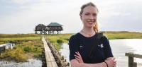 Vogelwartin Nele Waltering steht auf dem Anleger der Hallig Norderoog, im Hintergrund ist ihre Unterkunft zu sehen